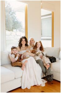 Family sits on couch together with big smiles for newborn photographer